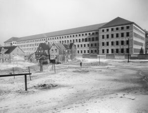 Der 1939 begonnene Neubau für das städtische Krankenhaus rechts der Isar kurz nach der Vollendung des Rohbaus. Die Kleinhausgruppe In der Grube 28 und 29 bildet vor diesem überdimensionierten Hintergrund nur noch den "schäbigen Rest" der einstigen Grubenbebauung, Aufnahme 1941. (Foto: Stadtarchiv München)  